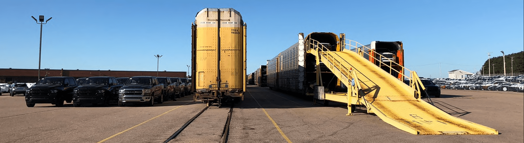 Autorack rail cars and a vehicle loading ramp at a CN rail terminal, with rows of vehicles staged for loading
